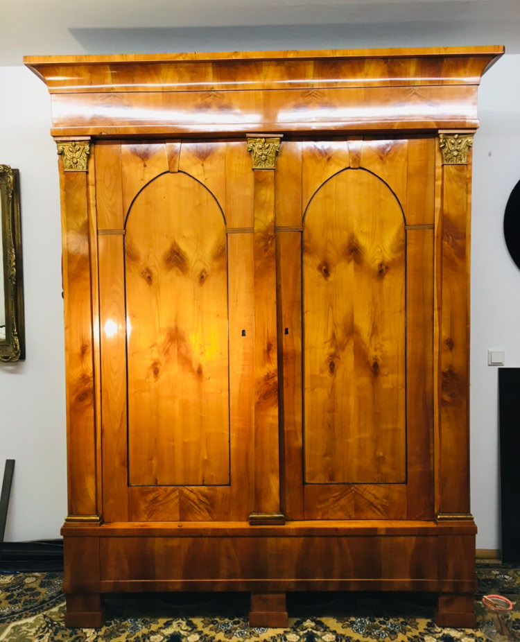 Großer, antiker Holzschrank mit zwei Türen und dekorativen Verzierungen, steht auf einem gemusterten Teppich.