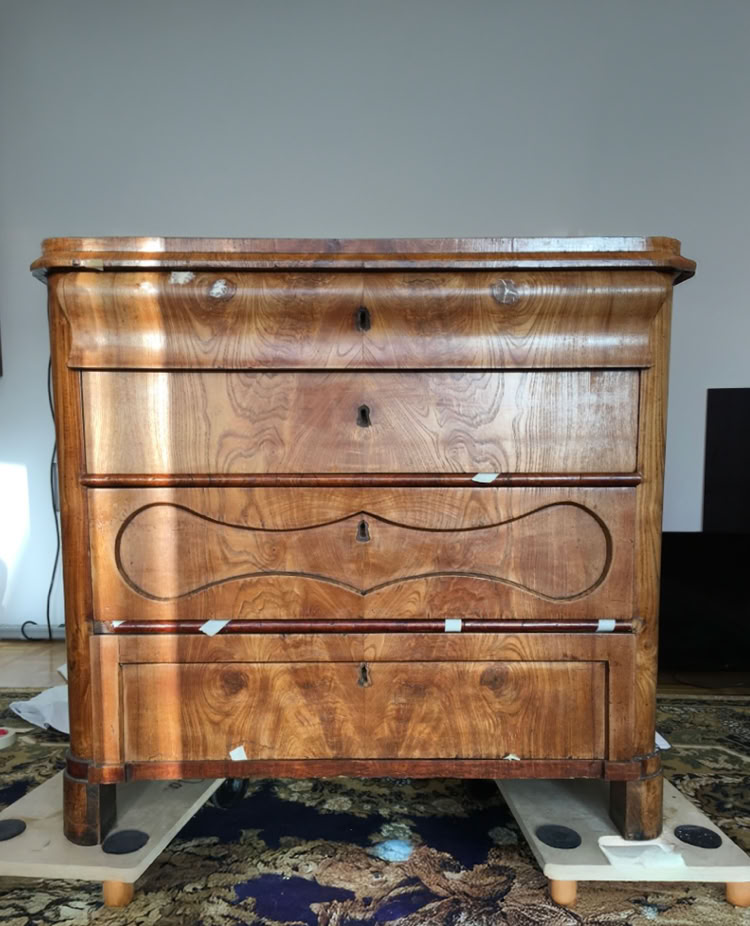 Holzkommode mit vier Schubladen, auf einem Teppich stehend.